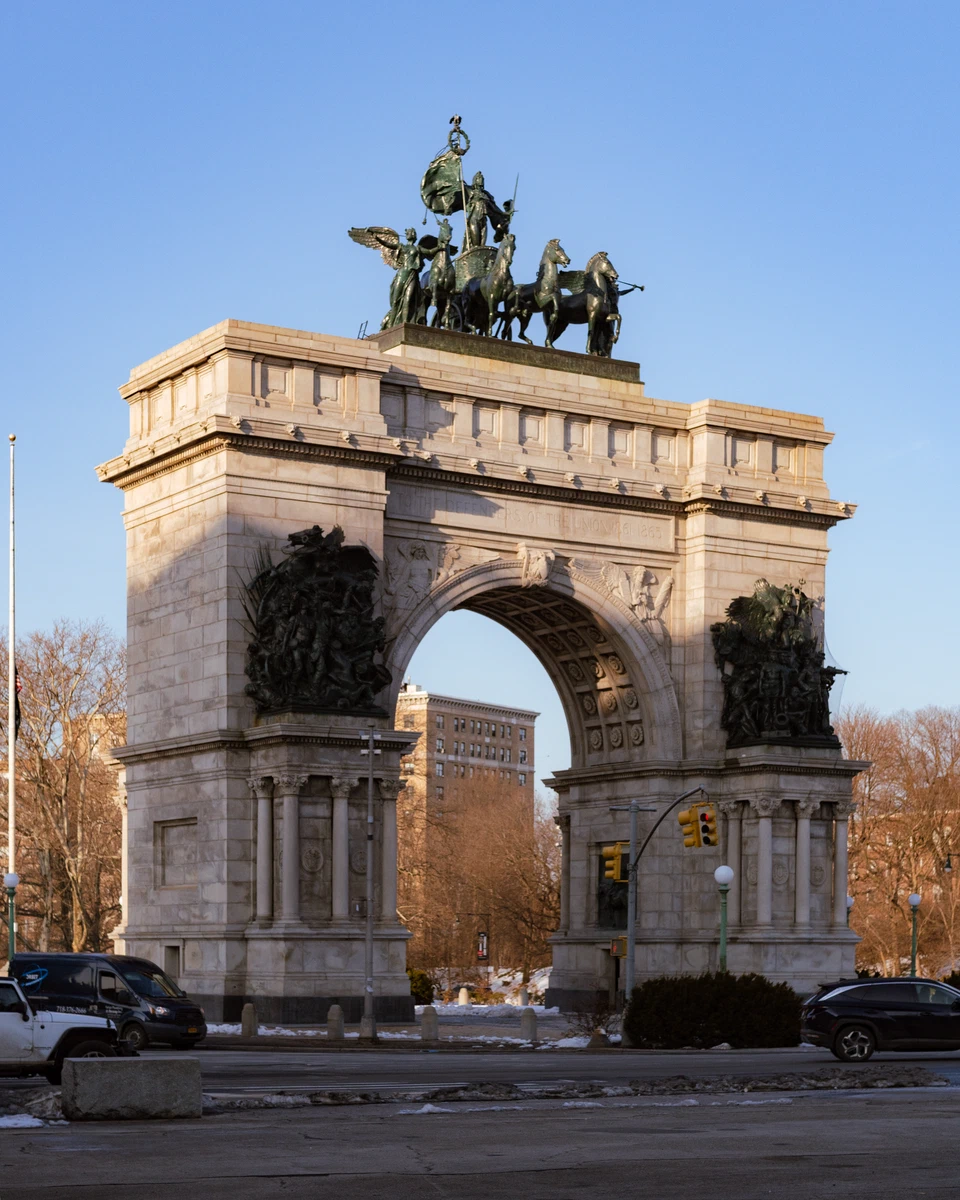The Soldiers' and Sailors' Memorial Arch at Grand Army Plaza, Brooklyn — a stone triumphal arch topped by a bronze chariot and horses, lit by low winter sun against a clear blue sky.